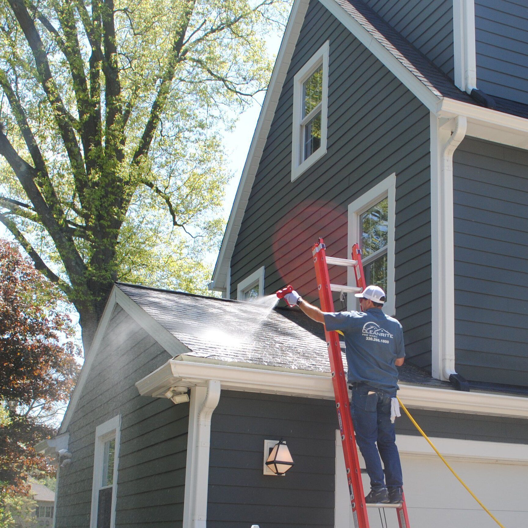 Worker pressure-washing two-story gray house